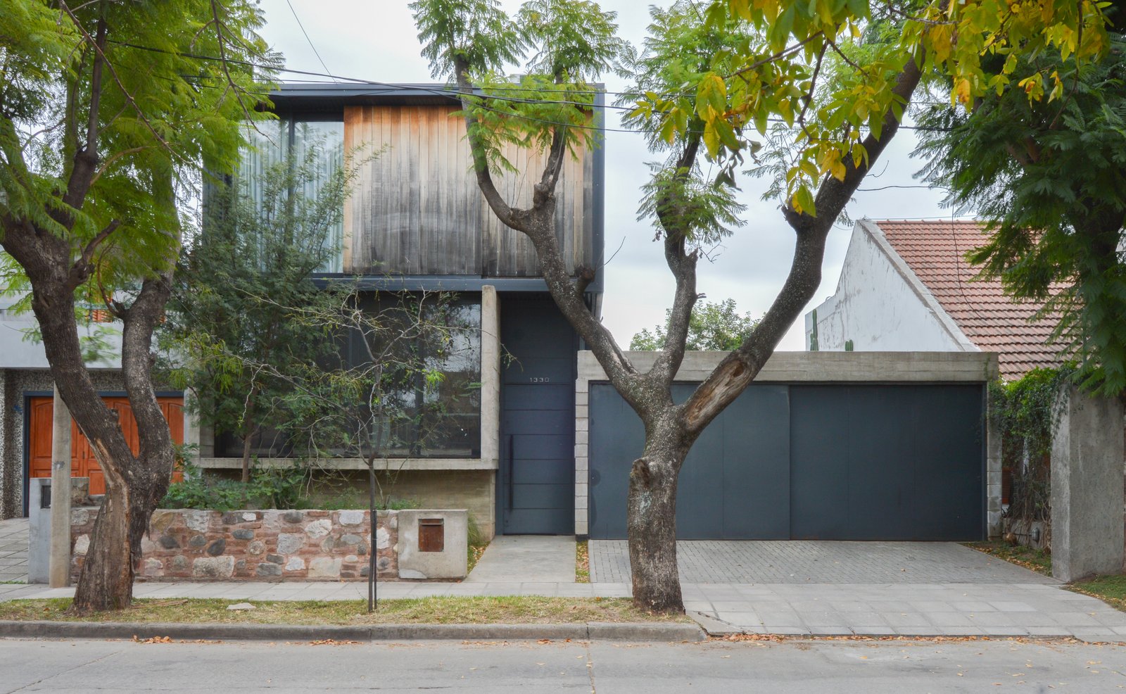 Fachada de casa moderna con revestimiento de madera y hormigón — proyecto CASA URRUTIA, por Sol Blanc. arquitecta, en Córdoba